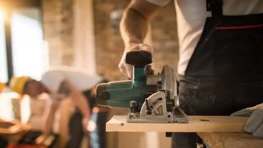 A man holding a power saw cutting through wood