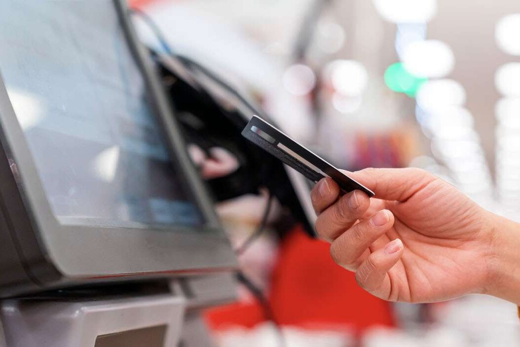 pos banner showing a consumer's hand with a credit card in it as she pays at a kiosk